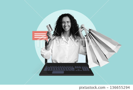 A woman smiles while holding shopping bags and a credit card. She is sitting in front of a laptop. The scene shows the activity of online shopping in a bright setting. 136655294