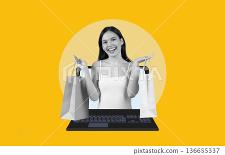 A woman smiles while holding shopping bags in each hand. She stands in front of a computer keyboard. The background is bright yellow, creating a lively atmosphere for online shopping. 136655337