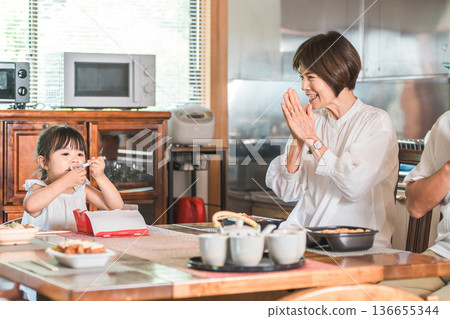 Senior couple eating with their granddaughter at the dining table (parents' home, three-generation family, meal, homecoming, returning home) 136655344