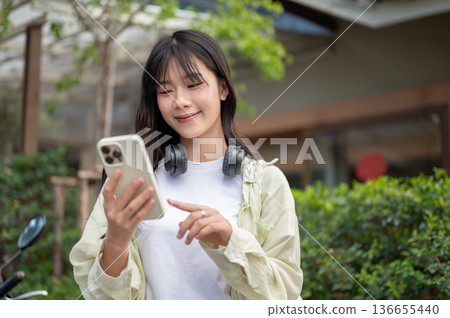 Pretty asian woman tourist looking at smartphone while standing or walking traveling by local road. Pretty asian woman tourist looking at smartphone while standing or walking traveling by local road. 136655440