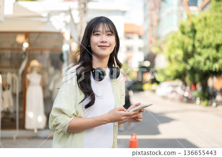 Pretty asian woman tourist holding smartphone while standing or walking around the local shop. Pretty asian woman tourist holding smartphone while standing or walking around the local shop. 136655443