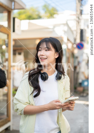 Pretty asian woman tourist looking away from smartphone while standing or walking around local shop. Pretty asian woman tourist looking away from smartphone while standing or walking around local shop. 136655444