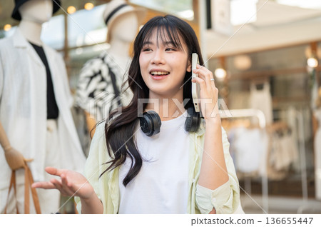 Pretty asian woman tourist talking on phone while standing or walking around the local clothing shop 136655447