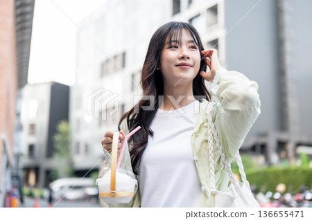 Smiling asian woman tourist holding cup holder with fresh coconut while standing or walking in mall Smiling asian woman tourist holding cup holder with fresh coconut while standing or walking in mall 136655471