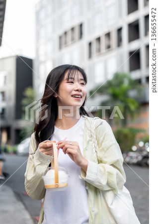 Happy asian woman tourist holding cup holder with fresh coconut while standing or walking in mall 136655472