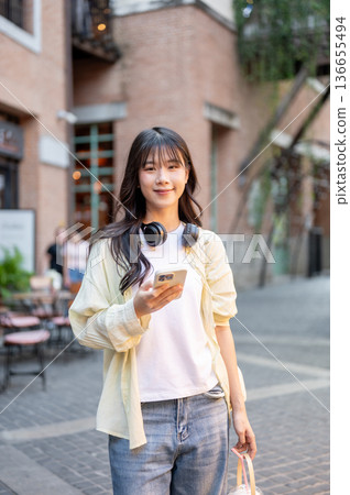 Asian woman tourist holding drink and phone while standing walking around in shopping mall or market Asian woman tourist holding drink and phone while standing walking around in shopping mall or market 136655494