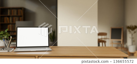 Blank screen laptop with book and pencil on wooden table across glass wall in a living room or cafe. 136655572