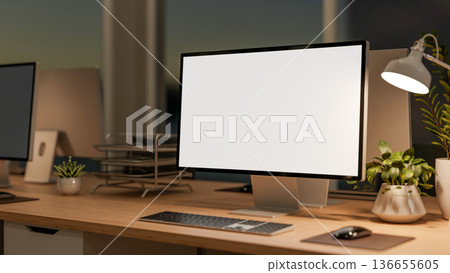White screen computer with potted plant and desk lamp on wooden working table in dim lit office room White screen computer with potted plant and desk lamp on wooden working table in dim lit office room 136655605