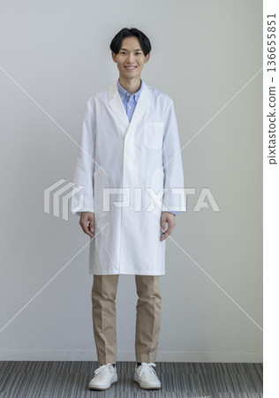 一位三十多歲的男子身穿白大褂，微笑著看向鏡頭，全身照，白色背景，肖像照 136655851