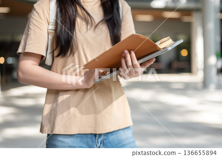 Close up of woman college student reading a book over laptop while standing or walking in a building Close up of woman college student reading a book over laptop while standing or walking in a building 136655894