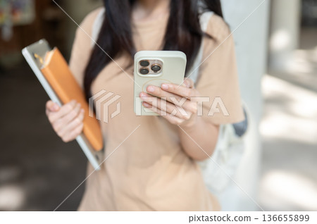 Close up of woman college student holding book looking at phone while standing walking in a building 136655899
