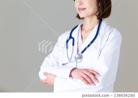 A middle-aged female doctor in a white coat with her arms folded 136656280