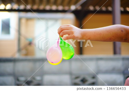 Close-up of a child's hand holding a water balloon in a summer park Close-up of a child's hand holding a water balloon in a summer park 136656433