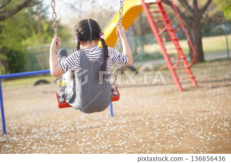 Back view of a girl on a swing in a spring park Back view of a girl on a swing in a spring park 136656436