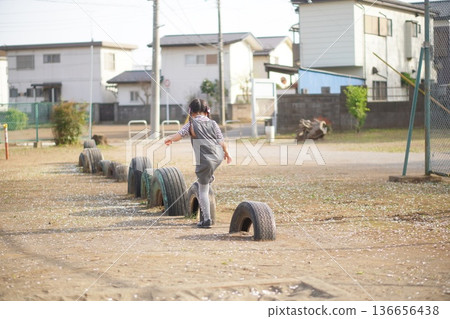 公園裡,一個女孩試圖走過一個輪胎,這是她的背影。 公園裡,一個女孩試圖走過一個輪胎,這是她的背影。 136656438