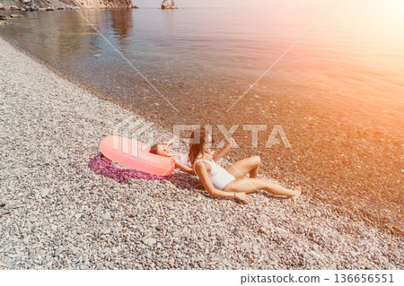 Mother child beach relaxing on a pebble shore with a pink inflatable ring during a sunny summer vacation Mother child beach relaxing on a pebble shore with a pink inflatable ring during a sunny summer vacation 136656551