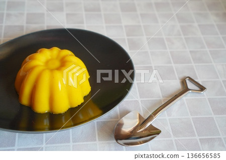 黑色盤子上盛著黃色果凍,配上一個可愛的湯匙。 黑色盤子上盛著黃色果凍,配上一個可愛的湯匙。 136656585