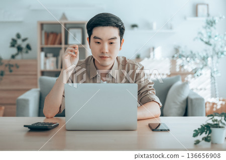 Happy young Asian man working on laptop in living room 136656908