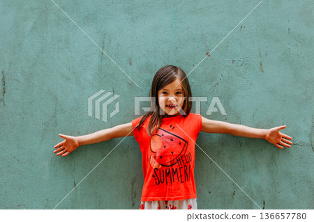 portrait of smiling girl in red t-shirt standing against green wall 136657780