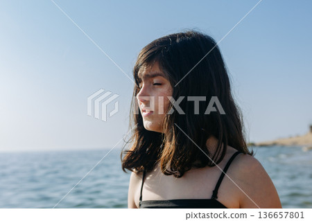 A close-up portrait of a teenage girl squinting in the sunlight. A close-up portrait of a teenage girl squinting in the sunlight. 136657801