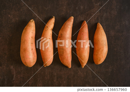 Sweet potatoes lined up on a dark surface ready for cooking or baking Sweet potatoes lined up on a dark surface ready for cooking or baking 136657960