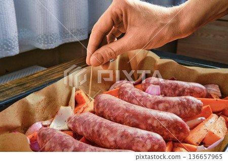 Hand inserting toothpick in natural casing sausages on a tray with vegetables in a kitchen setting 136657965