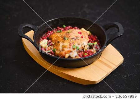Cooked chicken on a cast iron skillet served with red grain and green herbs in a dark setting Cooked chicken on a cast iron skillet served with red grain and green herbs in a dark setting 136657989