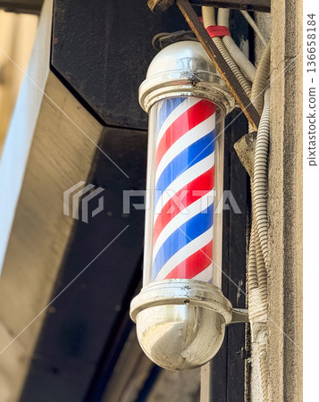 Close-up traditional barber pole with red, blue and white stripes mounted on a wall. Urban tradition, retro style and classic grooming culture. 136658184