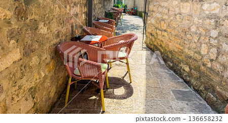 Outdoor cafe chairs along a narrow stone alley banner with copy space. Travel, leisure, lifestyle and relaxation in a historic European setting. Outdoor cafe chairs along a narrow stone alley banner with copy space. Travel, leisure, lifestyle and relaxation in a historic European setting. 136658232
