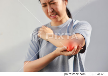 Young woman suffering from acute elbow pain and joint inflammation with red highlight effect, female touching sore arm, tendonitis, sports injury, arthritis, health problem, copy space background. Young woman suffering from acute elbow pain and joint inflammation with red highlight effect, female touching sore arm, tendonitis, sports injury, arthritis, health problem, copy space background. 136658329