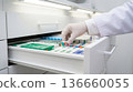 Pharmacist organizes medications in a drawer at a pharmacy during the day 136660055