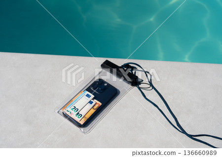 Waterproof pouch protecting smartphone and euro banknotes on a poolside, ensuring safety and security for valuables during summer vacation Waterproof pouch protecting smartphone and euro banknotes on a poolside, ensuring safety and security for valuables during summer vacation 136660989