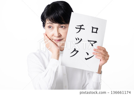 A senior woman is lost in thought, holding a piece of paper that says "Romantic" and putting her hand on her cheek A senior woman is lost in thought, holding a piece of paper that says "Romantic" and putting her hand on her cheek 136661174