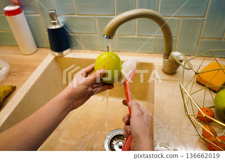 Focus on a childs hands thoroughly washing fresh, organic apples under flowing water, showcasing healthy habits and mindful food preparation. 136662019