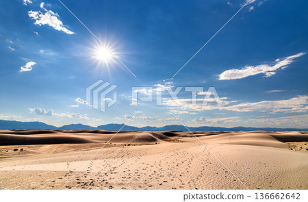 White Sands National Park in New Mexico. Scenic landscape features vast gypsum sand dunes with footprints leading toward mountains under a bright sunburst 136662642