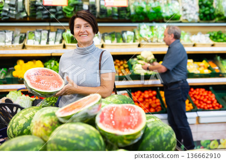 elderly woman chooses watermelon in fruit and vegetable section elderly woman chooses watermelon in fruit and vegetable section 136662910