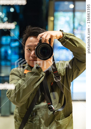 A photographer holds a camera and looks through the lens inside an indoor space. The image represents professional photography and visual content creation. A photographer holds a camera and looks through the lens inside an indoor space. The image represents professional photography and visual content creation. 136663395