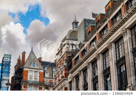 Classic British architecture lines a traditional London street, with red brick buildings and historic facades beneath a cloudy sky. 136663404