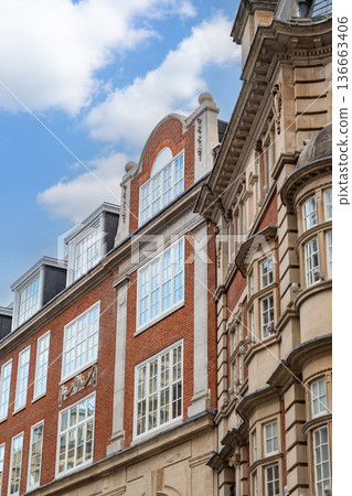 Classic British architecture lines a traditional London street, with red brick buildings and historic facades beneath a cloudy sky. 136663406