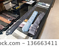 A customer compares two neckties on a glass counter inside a clothing store. The scene supports content about buying decisions and retail fashion choice. 136663411