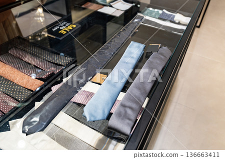 A customer compares two neckties on a glass counter inside a clothing store. The scene supports content about buying decisions and retail fashion choice. 136663411