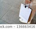 Person holding a blank paper shopping bag while walking outdoors. The clean surface allows flexible use for retail and commerce design. 136663416