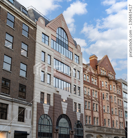 Classic British architecture lines a traditional London street, with red brick buildings and historic facades beneath a cloudy sky. 136663417