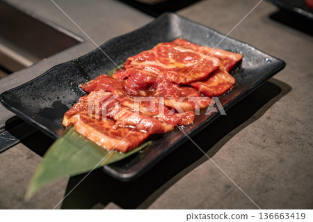 Raw sliced meat is arranged on a dark plate with visible fat texture, presented as uncooked food suitable for restaurant kitchen use and menu production. 136663419