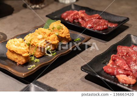 Multiple dishes served on dark plates including spicy salmon and raw meat. The table setting represents modern restaurant dining experience. 136663420
