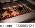 Beef slices cook on a metal grill with visible heat and browning surface, reflecting a professional restaurant environment and active food preparation process. 136663424