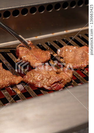 Beef slices cook on a metal grill with visible heat and browning surface, reflecting a professional restaurant environment and active food preparation process. Beef slices cook on a metal grill with visible heat and browning surface, reflecting a professional restaurant environment and active food preparation process. 136663425