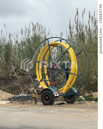 Agricultural irrigation equipment with yellow hose reel, standing on a rural road background Agricultural irrigation equipment with yellow hose reel, standing on a rural road background 136663746
