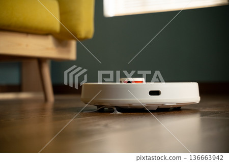Robot vacuum moving across a shiny wooden floor, cleaning the surface with its rotating brushes, providing convenient smart home technology for daily chores Robot vacuum moving across a shiny wooden floor, cleaning the surface with its rotating brushes, providing convenient smart home technology for daily chores 136663942