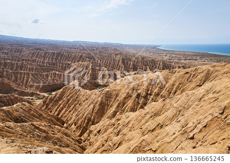 Aksai Canyon landscape with rugged terrain and distant sea. Natural erosion forming patterns in Kyrgyzstan desert. Geological formation. 136665245